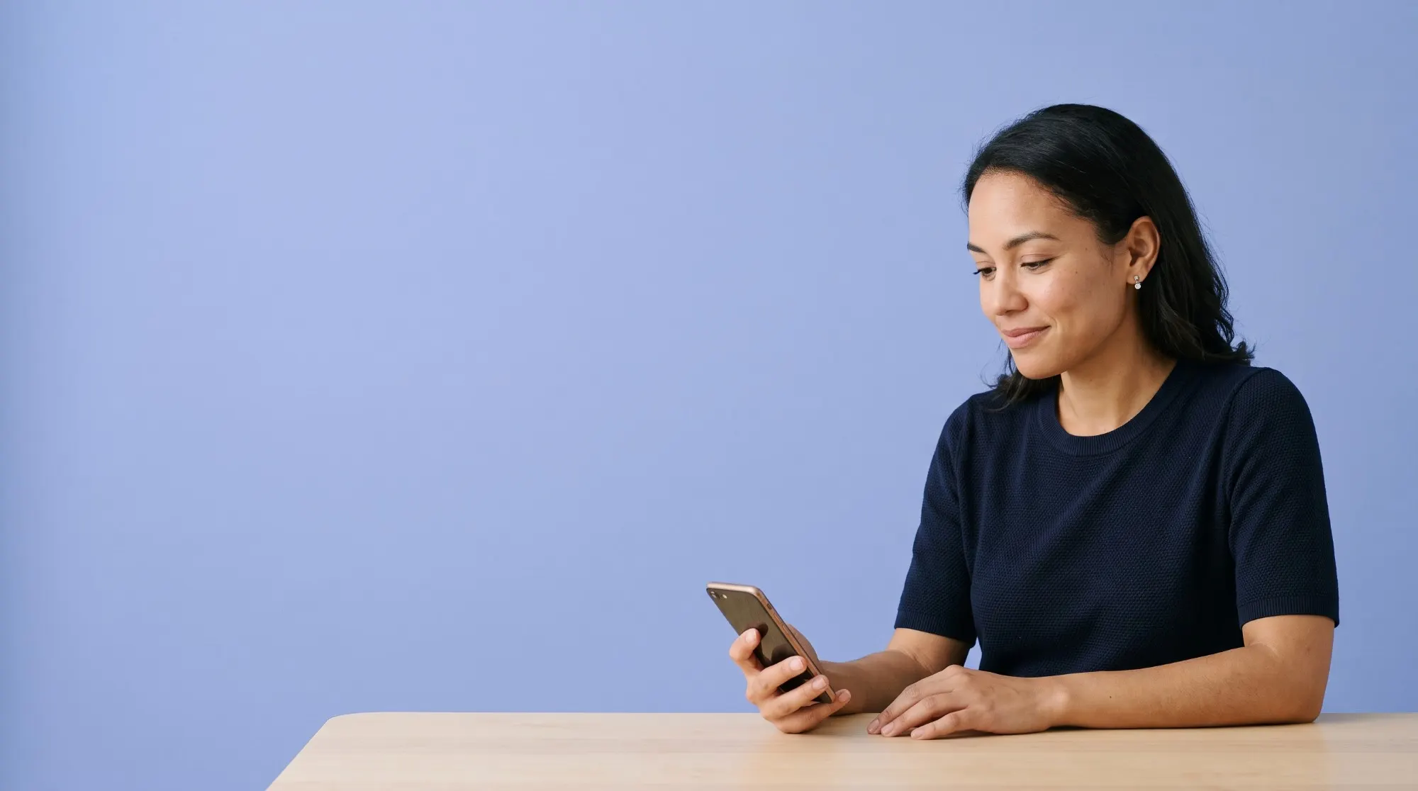 A woman at a table, smiling at something on her phone