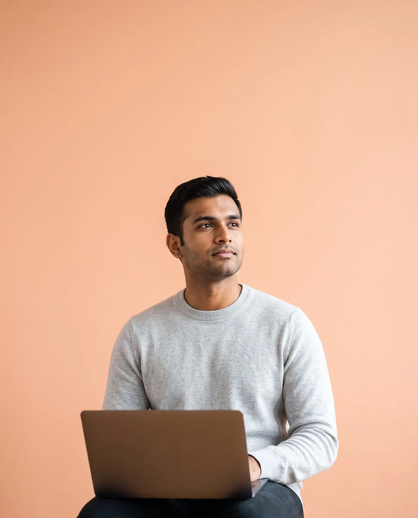 A man with a laptop on his knees, looking up thoughtfully